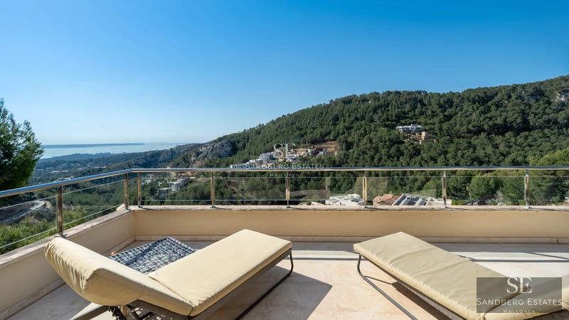 Modern living room with large windows, sea view, and designer furniture. Beige sofa, wood coffee table, and minimalist decoration.