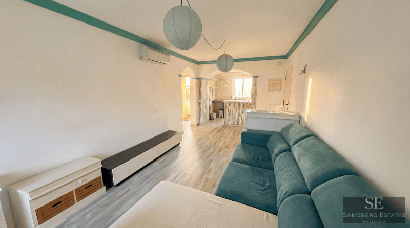 A living room featuring a turquoise sofa, wooden floors, and spherical paper lanterns next to an archway.