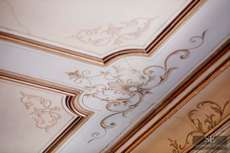 Close-up of ornate ceiling molding with hand-painted floral filigree in cream and gold.