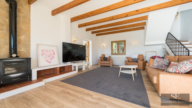 Cozy living room featuring exposed wood beams, a black wood-burning stove, tan leather sofas, and a large TV.