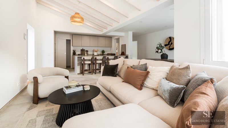 Bright living room with beige sofa, wooden ceiling beams, and a modern kitchen island in the background.