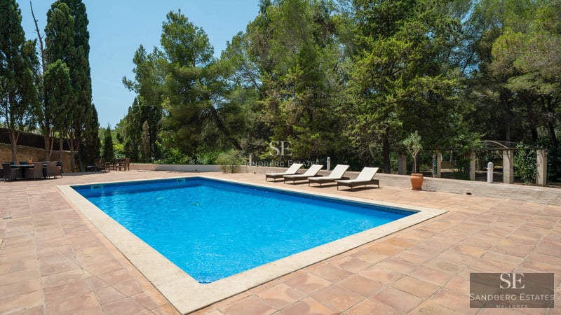 Vista exterior de una villa moderna con piscina infinita. Fachada de piedra, amplios ventanales y paisajismo elegante.