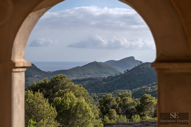 A view of lush green mountains and the distant sea framed by a traditional stone archway.