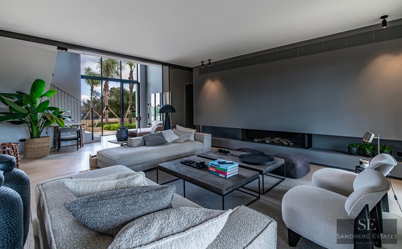 Spacious modern living room featuring gray sectional sofas, a built-in fireplace, and large windows framing palm trees.