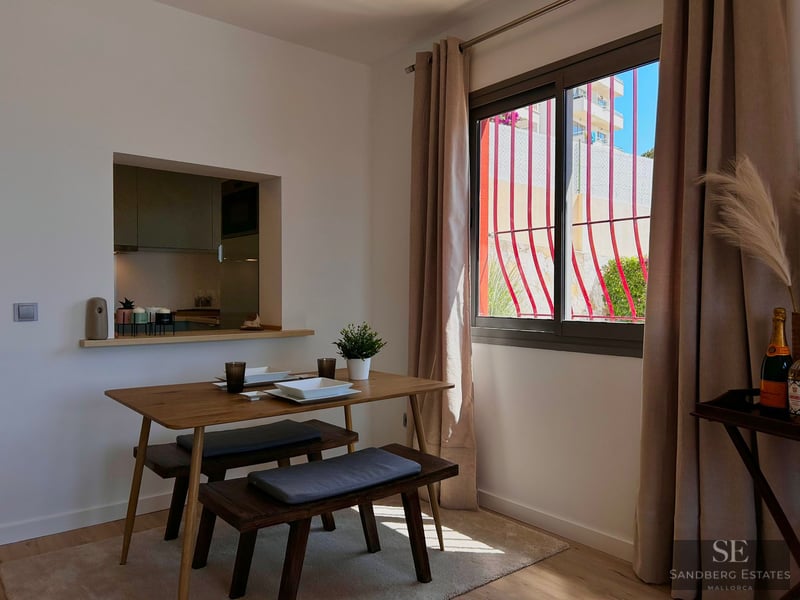 Minimalist dining room with a wooden table, benches, and a window view of red decorative bars.