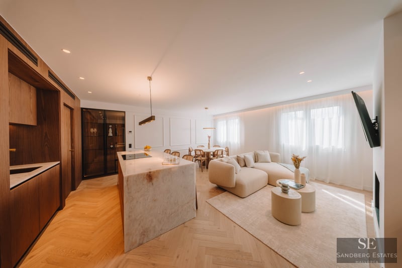 Modern open-plan living room with marble kitchen island, beige sectional sofa, and light wood herringbone floors.