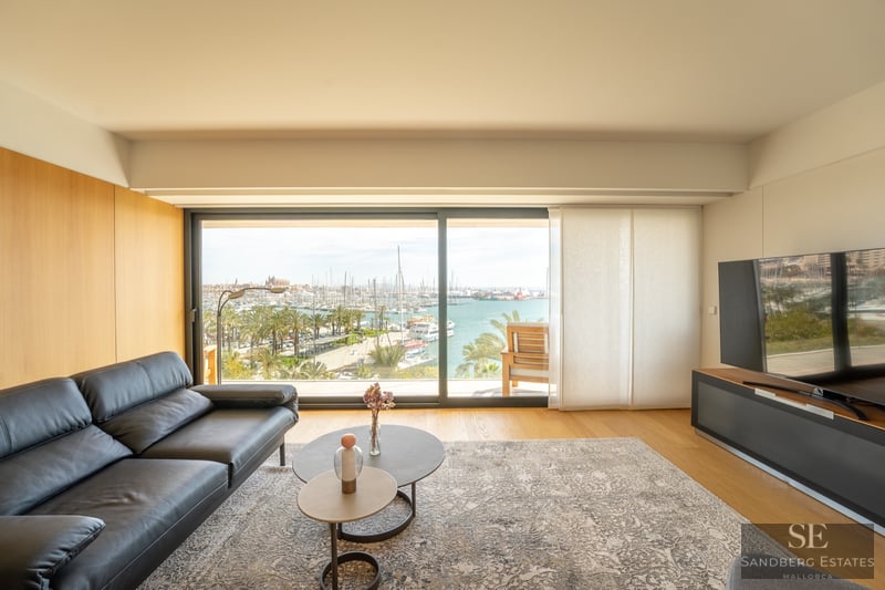 Modern living room featuring a black leather sofa and large glass sliding doors overlooking a harbor with many boats.