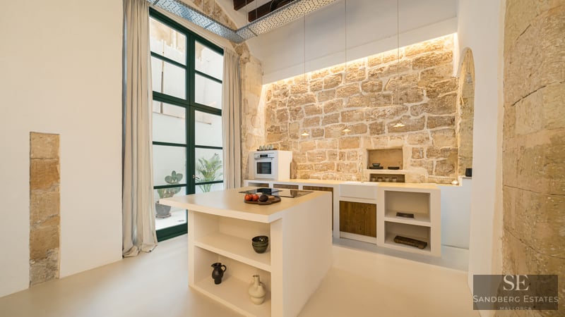 Contemporary kitchen featuring a white island, rustic stone wall, high ceilings, and large windows.