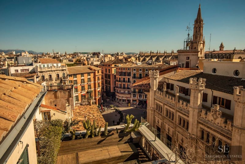 High-angle view of Mediterranean city rooftops and a Gothic cathedral spire under a bright blue sky.