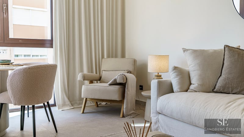 Helle Wohnzimmerecke mit cremefarbenem Sofa, Sessel, Bouclé-Stuhl und weichen, bodentiefen Vorhängen.