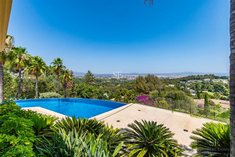 Wide view of modern villa featuring an infinity pool, sea views, minimalist design, large terraces and elegant outdoor furniture.