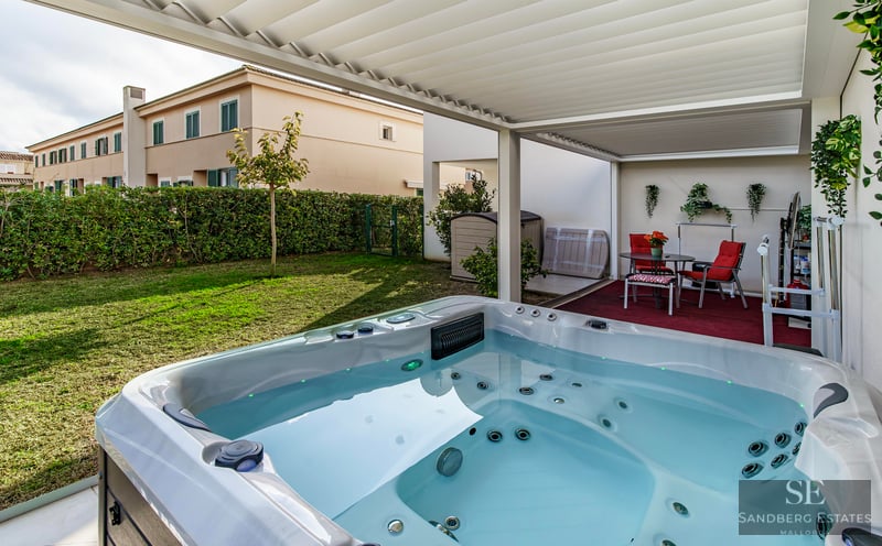 White luxury hot tub under a slatted pergola overlooking a private green garden and outdoor seating area.