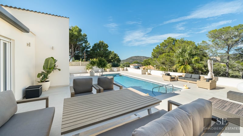 Grande terrasse ensoleillée avec une piscine rectangulaire, mobilier de salon élégant et cadre verdoyant.