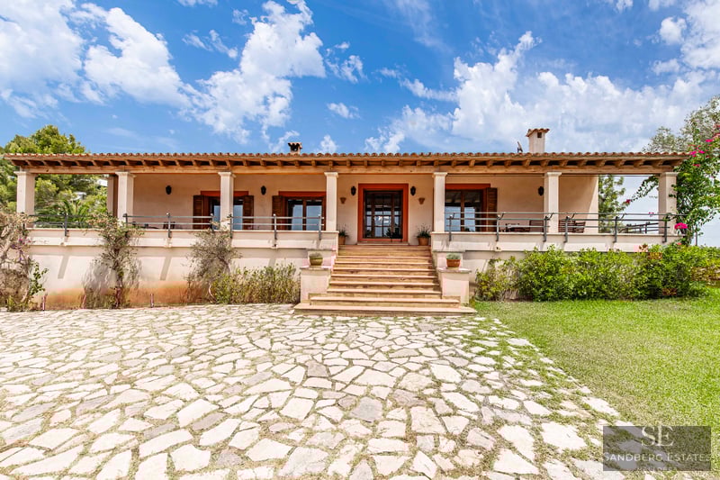 Vista frontal de una villa mediterránea de una planta con entrada de piedra, escaleras y terraza cubierta.