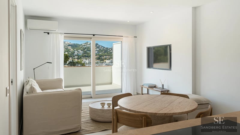 Spacious living room featuring expansive windows, designer sofas, a fireplace, and panoramic sea views. Natural lighting and hardwood floors.