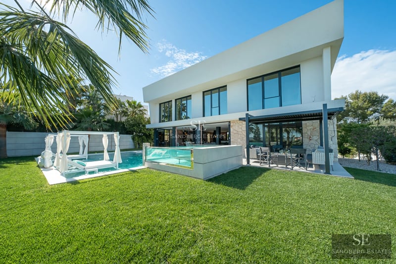Spacious living room with panoramic windows, ocean view, light wood floors, fireplace, and modern furniture in neutral tones.