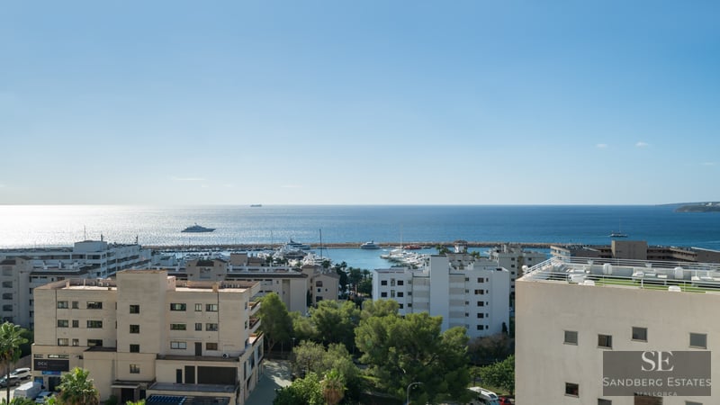 High-angle view of a coastal city, a yacht-filled marina, and the vast blue Mediterranean Sea under a bright sky.