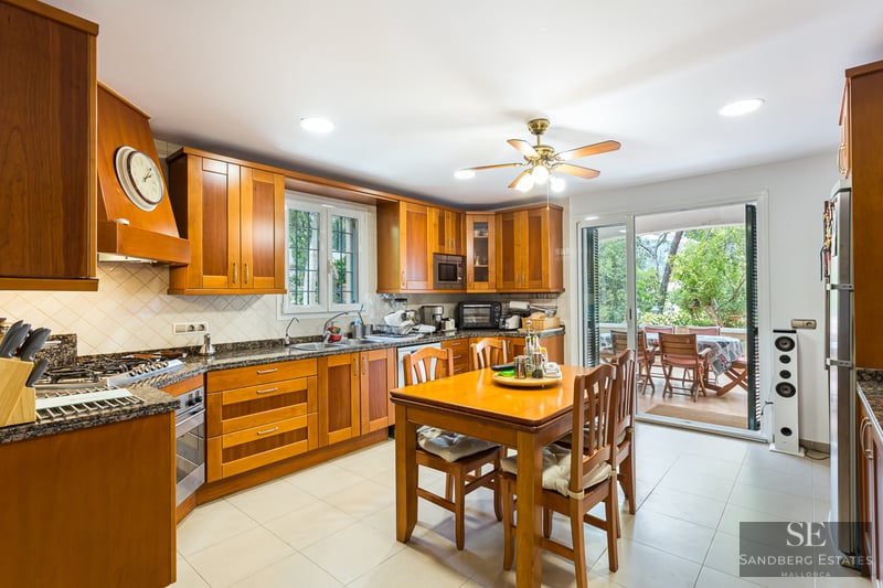 Traditional wooden kitchen with granite counters, dining table, and glass doors leading to a terrace.