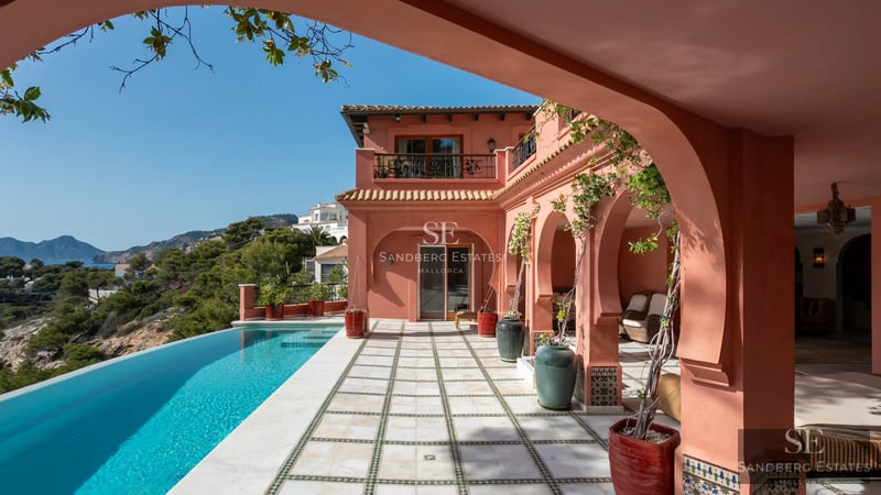 Pool view with sun loungers and umbrellas. Modern building with large windows reflecting sunlight. Landscaped garden.