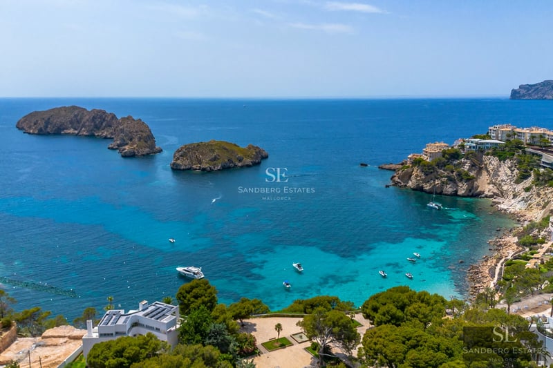 View of a luxurious infinity pool with stone edging, modern sun loungers, and lush greenery. Minimalist architecture, blue sky.