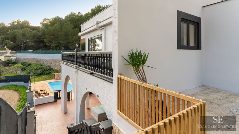 Villa blanche à plusieurs niveaux avec balustrades noires et en bois, surplombant une piscine turquoise et la forêt.