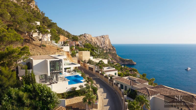 Modern living room with large windows, grey sofas, light rug and panoramic sea views. Abundant natural lighting.