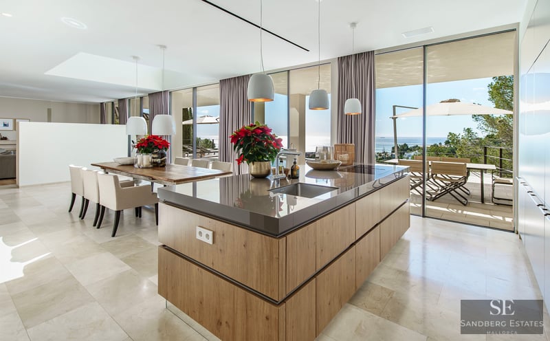 Modern kitchen featuring a wooden island, marble floors, and floor-to-ceiling glass walls overlooking the sea.