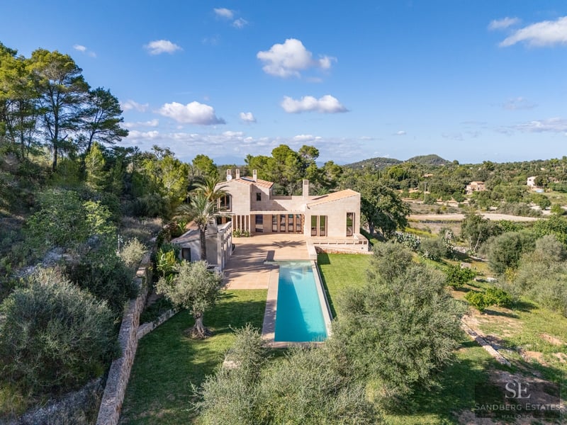 Aerial-style view of a modern stone villa with a long turquoise lap pool surrounded by lush Mediterranean trees.