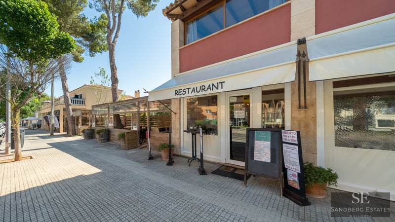 Exterior view of a restaurant with stone walls, white awnings, and a tree-lined sidewalk under a clear sky.
