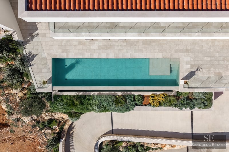 Bird's eye view of a turquoise swimming pool, stone terrace, terracotta roof, and lush Mediterranean landscaping.
