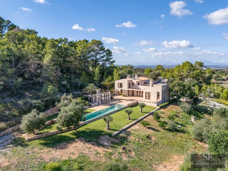 Aerial view of a luxury stone villa with a long turquoise pool surrounded by olive trees and lush forest.