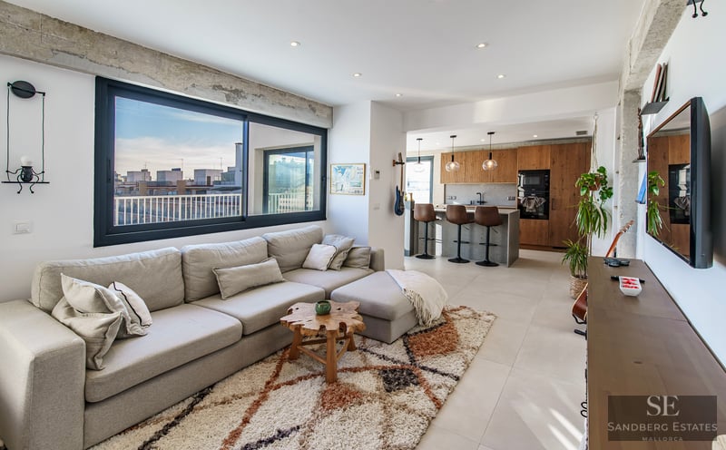 Bright modern living room with a large gray sectional sofa, textured rug, and an open kitchen with city views.
