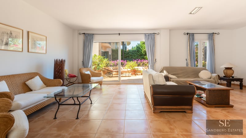 Spacious living room featuring wicker sofas, terracotta tiling, and large sliding glass doors opening to a sunny terrace.