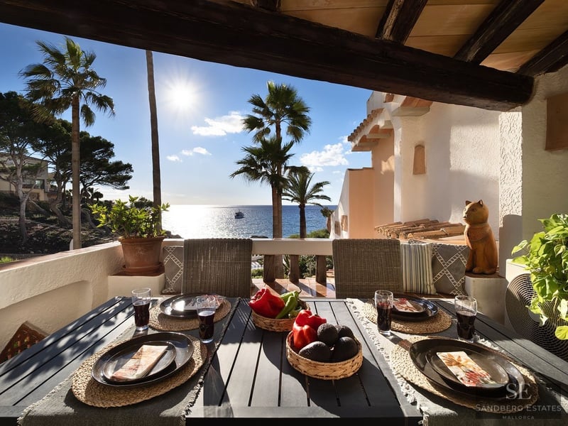 Mesa de comedor exterior preparada en una terraza soleada con vistas al mar Mediterráneo y palmeras.