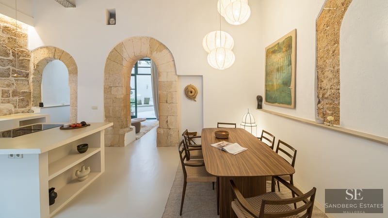 Modern wooden dining table under globe pendant lights, framed by authentic stone arches in a bright white space.