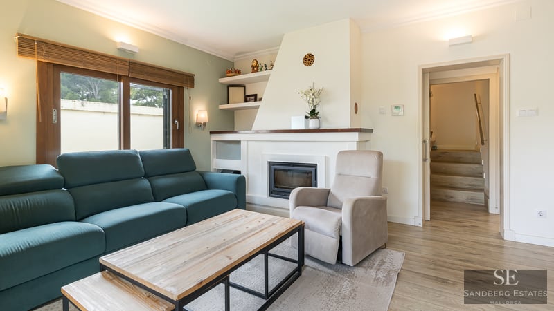 Modern living room with a teal sofa, white built-in fireplace, wooden coffee table, and beige armchair.