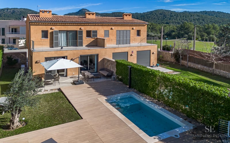 Aerial view of an ochre-colored villa featuring a swimming pool, wooden deck, garden, and hills in the background.