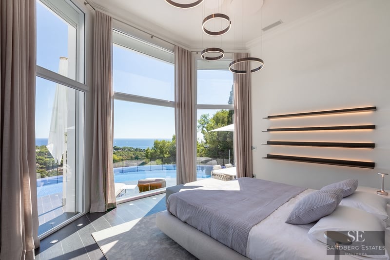 Modern master bedroom with floor-to-ceiling windows overlooking an infinity pool and the Mediterranean sea.