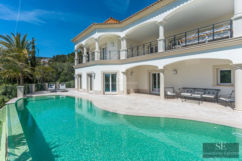 Exterior view of a luxurious apartment featuring a pool, terrace with sun loungers, and green spaces. Sleek modern design with soft lighting.