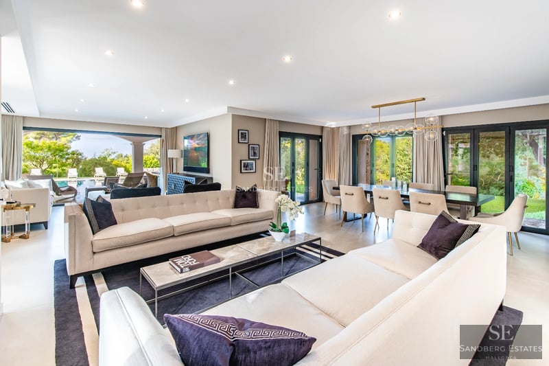 Spacious pool bordered by lush greenery and a modern villa with large windows reflecting sunlight.