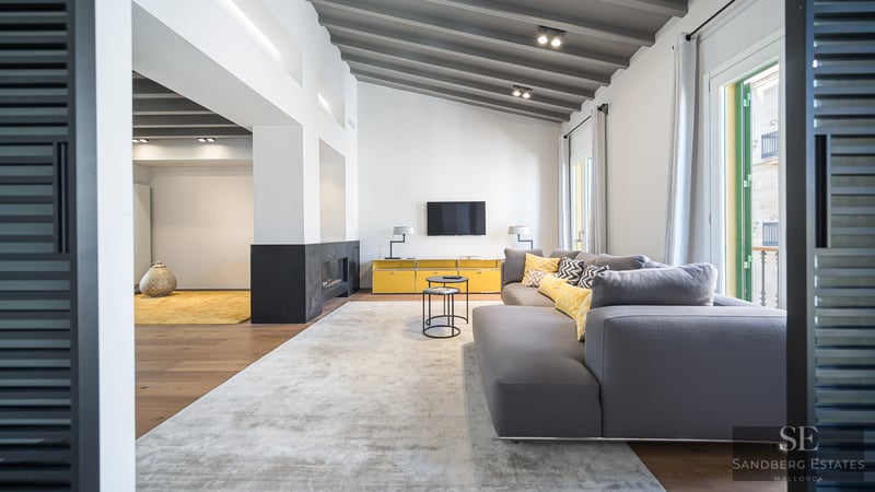 Geräumiges Wohnzimmer mit grauem Sofa, gelben Möbeln, Kamin und Sichtbalkendecke.