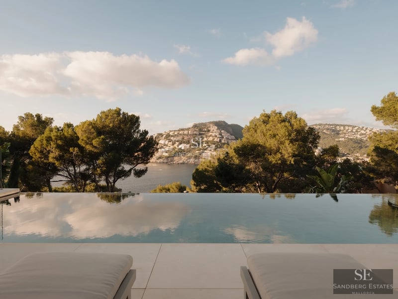 Spacious living room with large windows, light wood floors, a modern fireplace, and views of the garden with a pool. Minimalist and bright design.