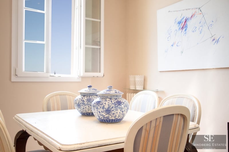 Heller Essbereich mit weißem Tisch, zwei blau-weißen Porzellangefäßen und offenem Fenster mit Blick auf den blauen Himmel.