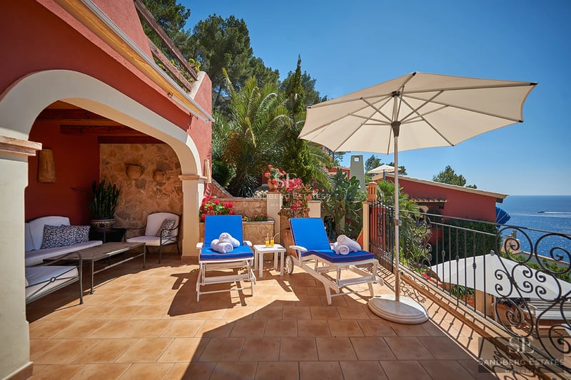 View of a modern villa featuring an infinity pool, expansive terraces, and lush gardens. Minimalist design with large windows.