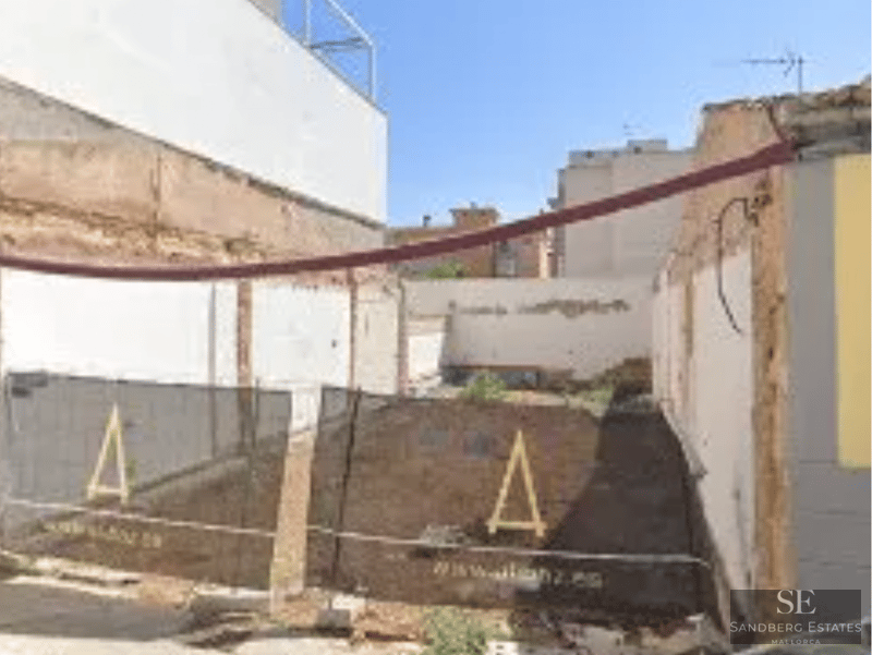 Vy över en byggarbetsplats med säkerhetsstängsel och synliga vita grundmurar.