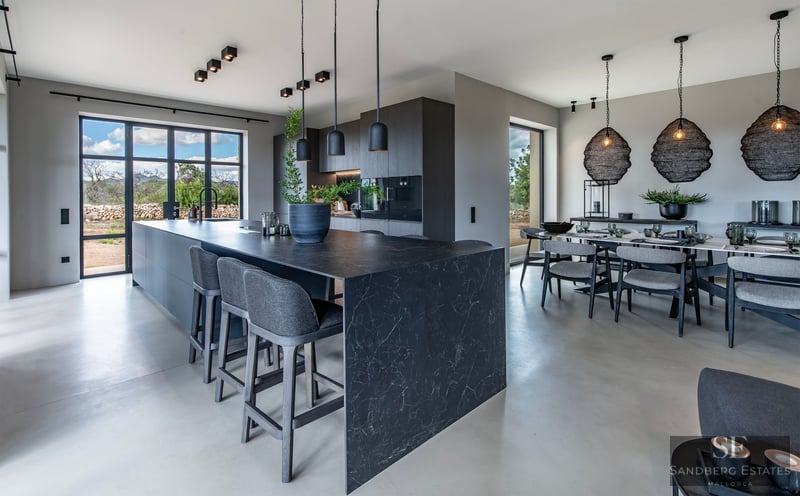 Modern open-plan kitchen with a dark marble island, grey stools, and a dining table under black designer pendant lights.