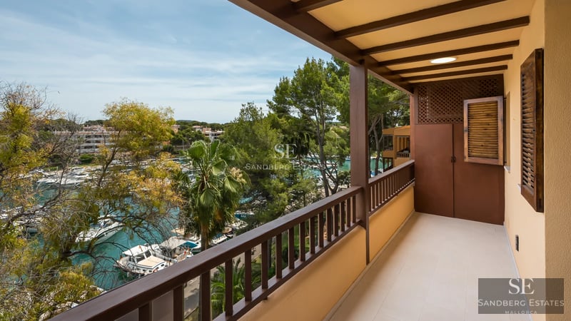 View of an infinity pool with turquoise water, bordered by light tiles. A modern house with large windows in the background.
