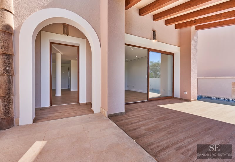 Covered terrace with stone floors, wooden beams, an arched entry, and a pool on the right side.