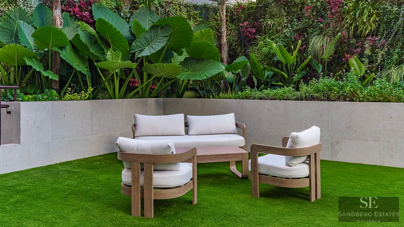 Moderne Holz-Terrassenmöbel auf grünem Rasen vor einer Steinwand und üppigen tropischen Pflanzen.