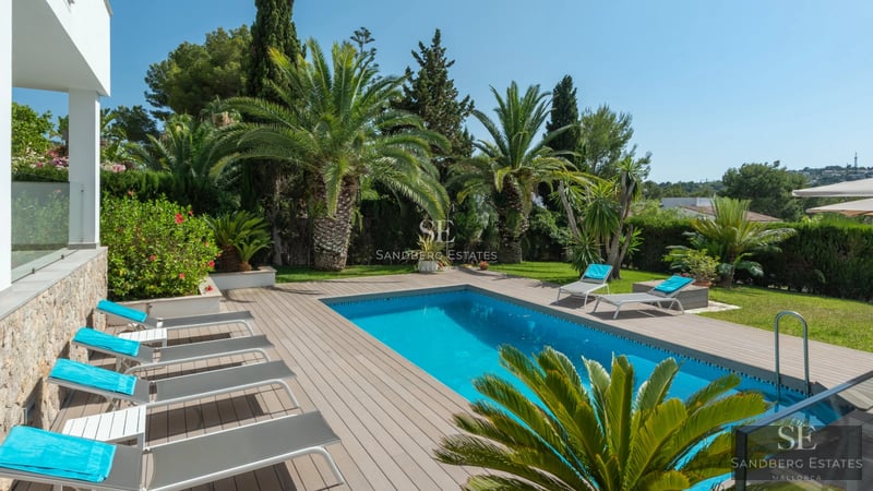 Exterior view of modern villa with infinity pool, wooden terrace, large glass windows, and lush garden. Contemporary architectural design.